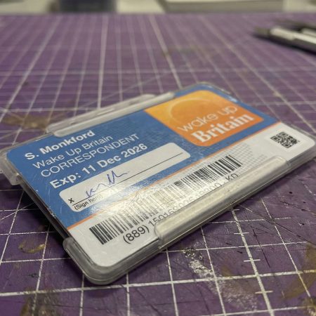 Close-up of a Wake Up Britain conference ID badge with a barcode and expiry date, placed on a purple craft cutting mat.